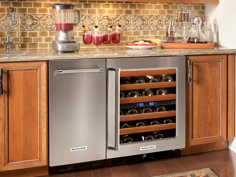 A black KitchenAid® ice maker next to an open wine cooler in a modern kitchen