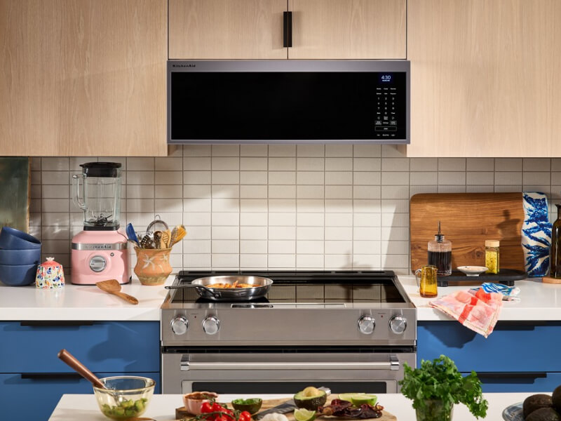 Electric range below a low profile microwave in a kitchen with tan cabinetry