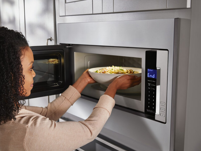 Person taking a bowl of pasta out of a built-in microwave