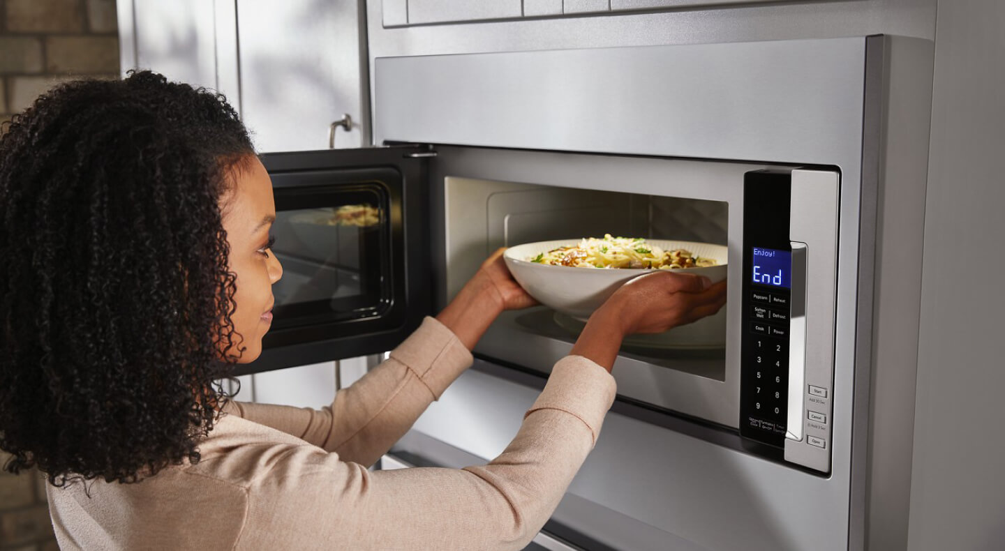 Person taking a bowl of pasta out of a built-in microwave