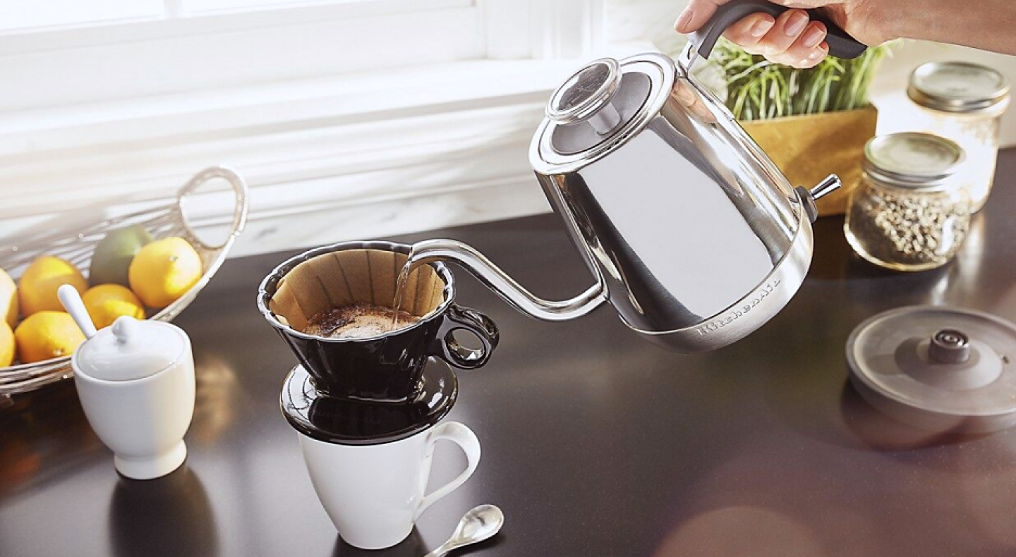 Maker pouring boiled water from gooseneck kettle into filter for pour over coffee