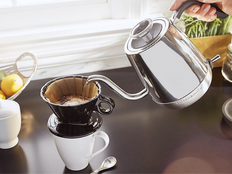 Maker pouring boiled water from gooseneck kettle into filter for pour over coffee