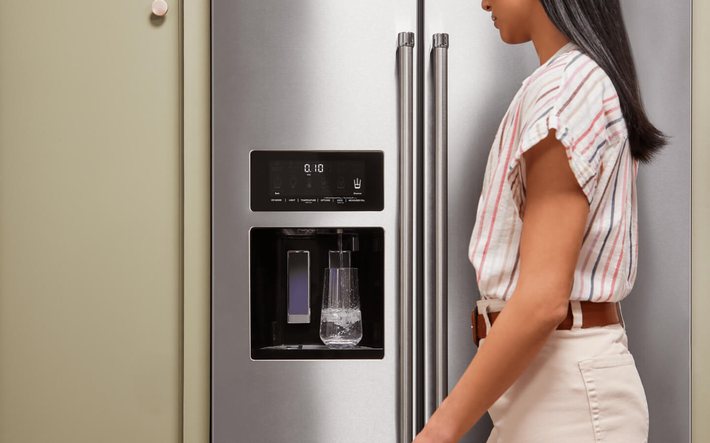 A person filling a glass of water using their refrigerator’s interior water dispenser