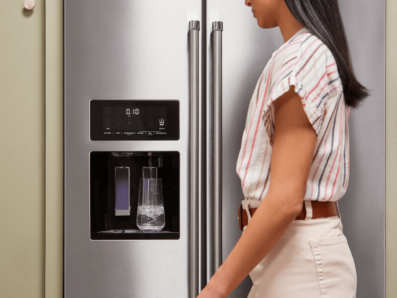 A person filling a glass of water using their refrigerator’s interior water dispenser
