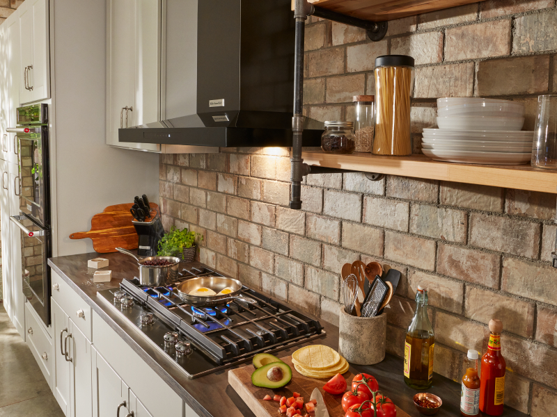 Black KitchenAid® canopy range hood over gas stovetop with brick backsplash