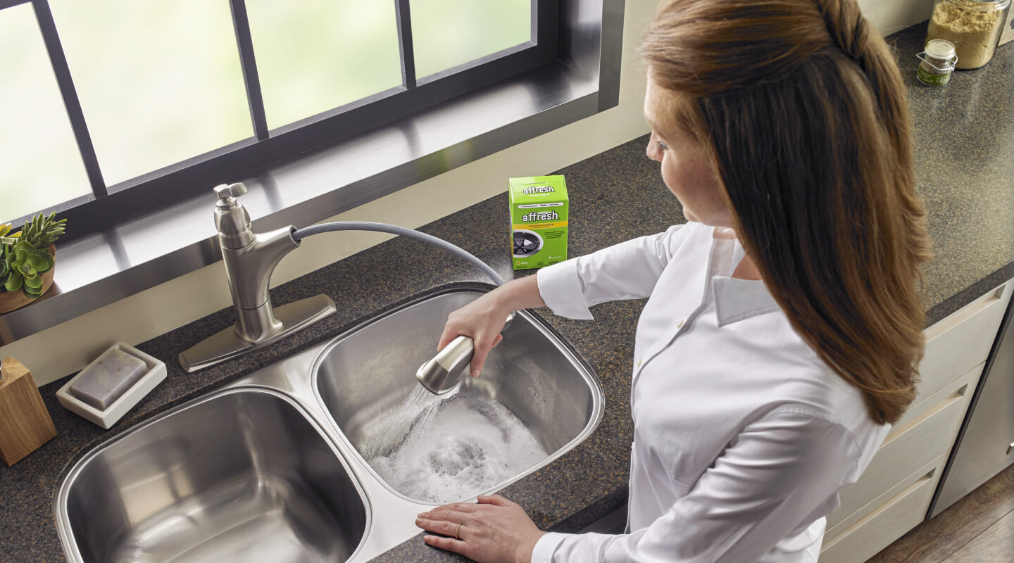 A person using affresh® Disposal Cleaner in a double sink