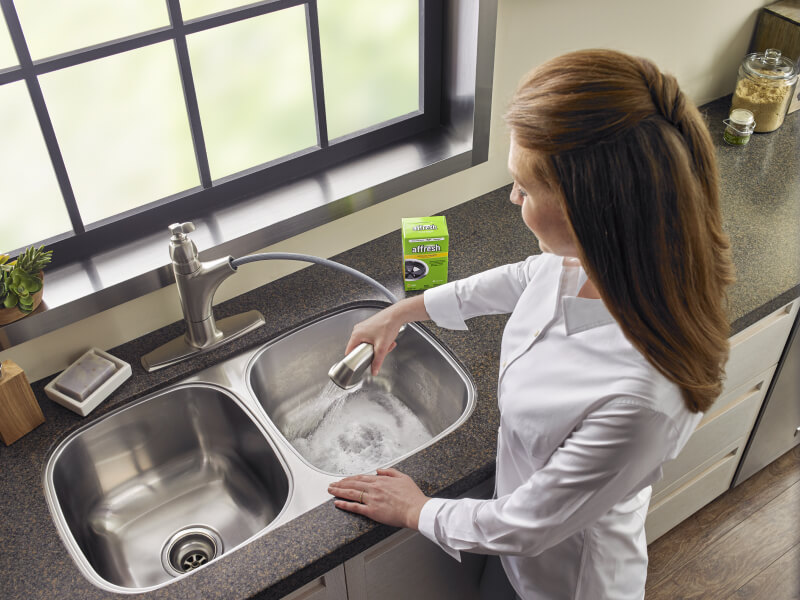A person using affresh® Disposal Cleaner in a double sink