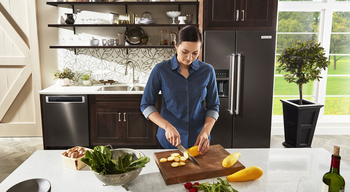 A person cutting vegetables in a kitchen with black stainless steel appliances