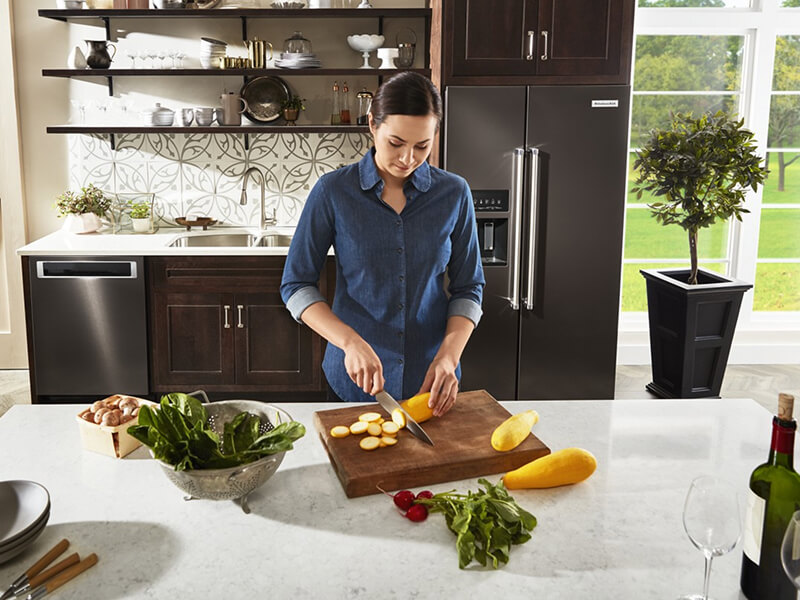 A person cutting vegetables in a kitchen with black stainless steel appliances