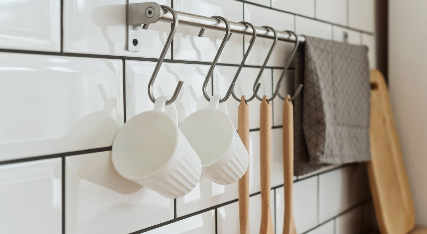 Mugs and wooden mixing spoons hanging from hooks on a rod