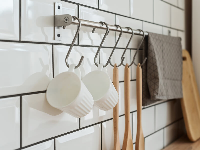 Mugs and wooden mixing spoons hanging from hooks on a rod