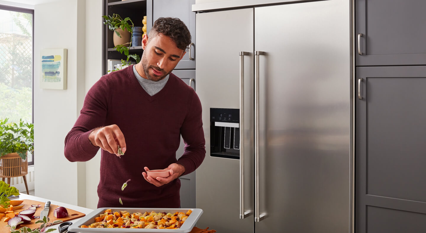 Person seasoning food in front of a stainless steel side-by-side refrigerator
