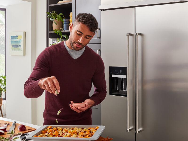 Person seasoning food in front of a stainless steel side-by-side refrigerator