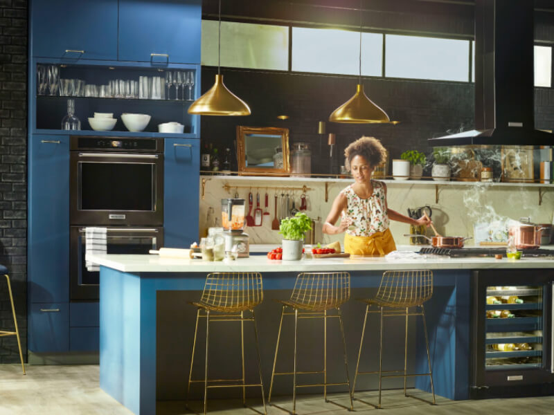 Person cooking in a kitchen with deep blue cabinets and black stainless steel KitchenAid® appliances