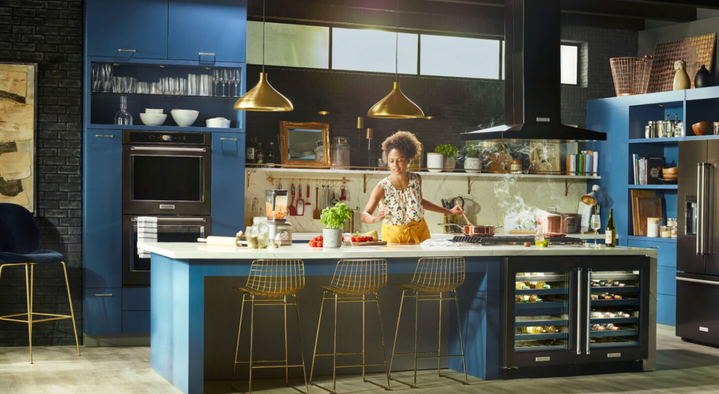 Person cooking in a kitchen with deep blue cabinets and black stainless steel KitchenAid® appliances