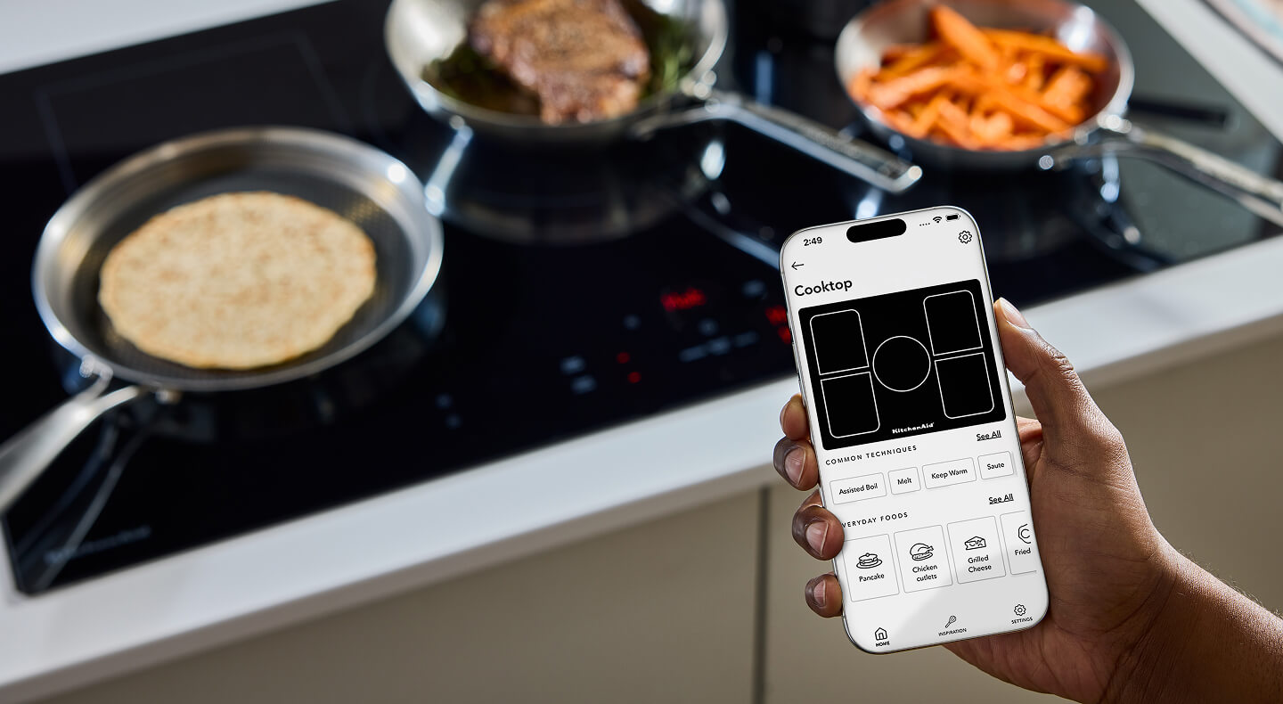 A person holding a phone in front of a KitchenAid® cooktop
