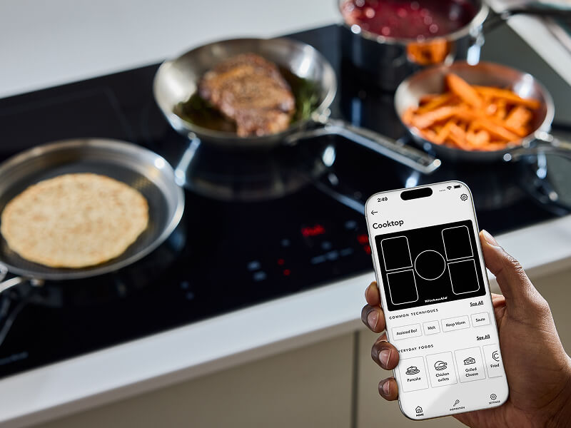 A person holding a phone in front of a KitchenAid® cooktop