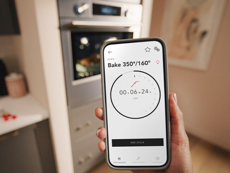 A person holding a phone in front of a KitchenAid® wall oven