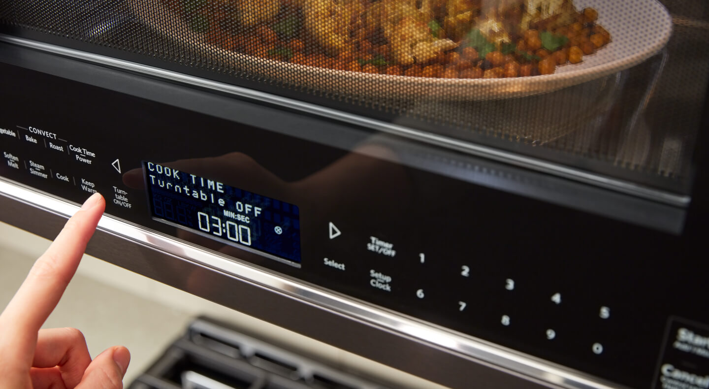A person programming a setting on a KitchenAid® microwave