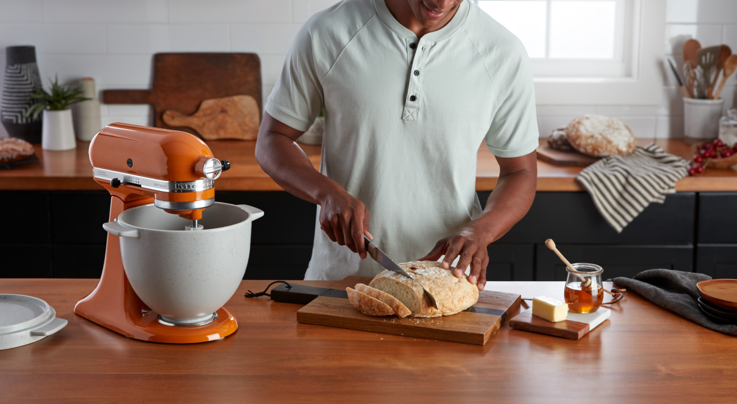 Person slicing bread next to orange stand mixer