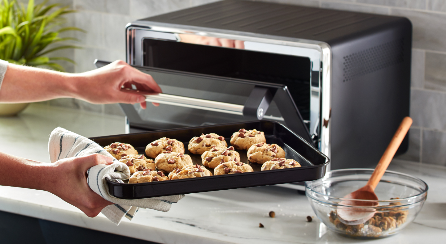Person placing a tray of cookies into a KitchenAid® countertop oven