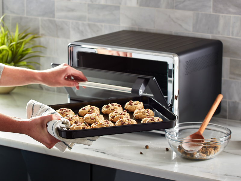 Person placing a tray of cookies into a KitchenAid® countertop oven