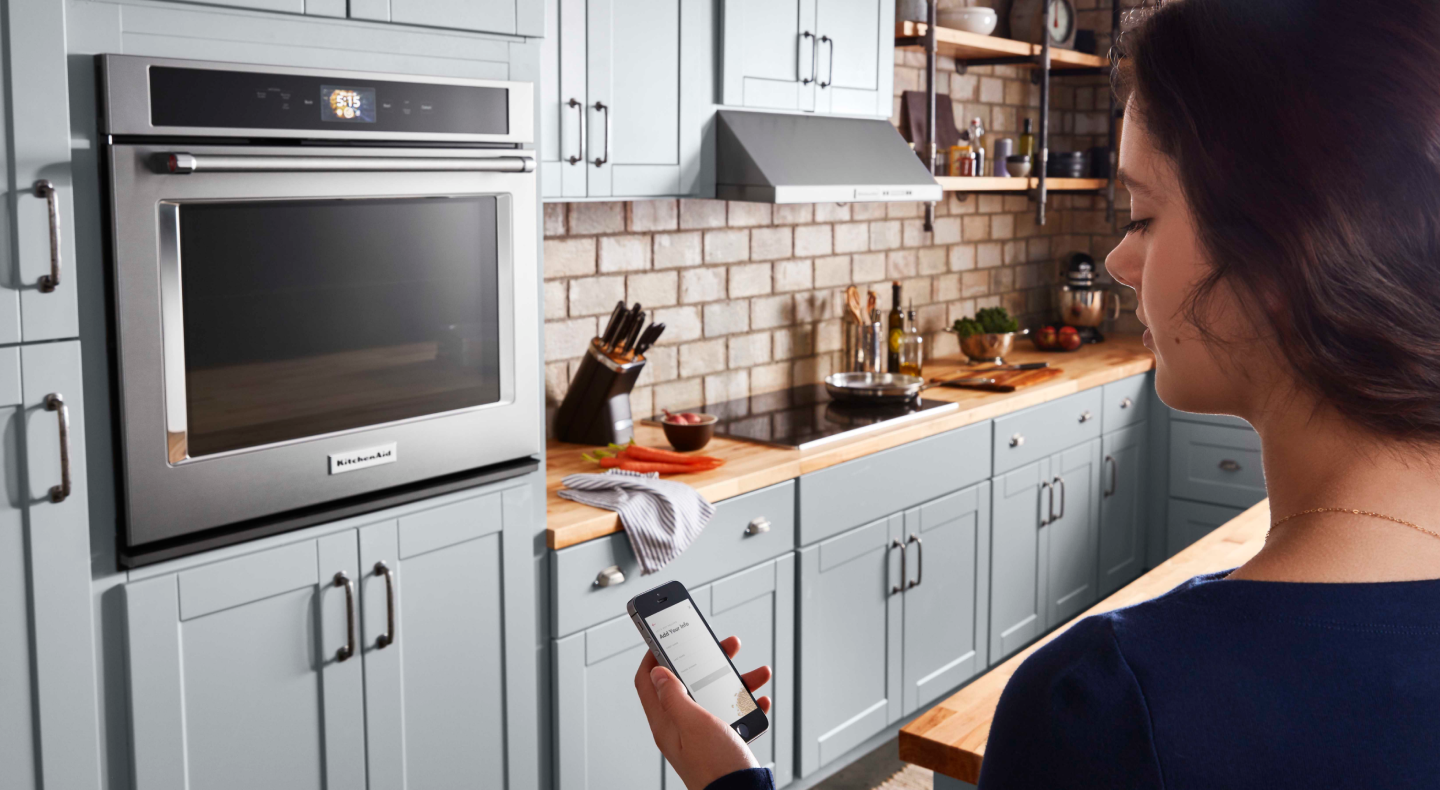A woman checking a smartphone to control a smart oven