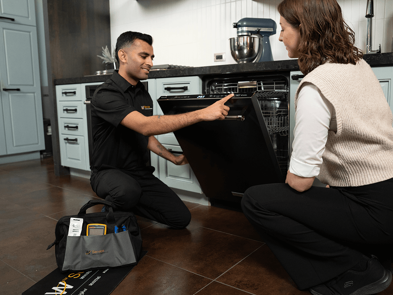 A technician helps a woman with her dishwasher