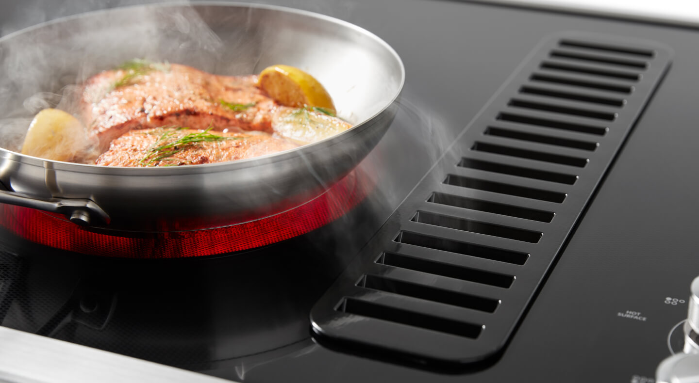 Salmon cooking on a downdraft electric range with a lit up red element 