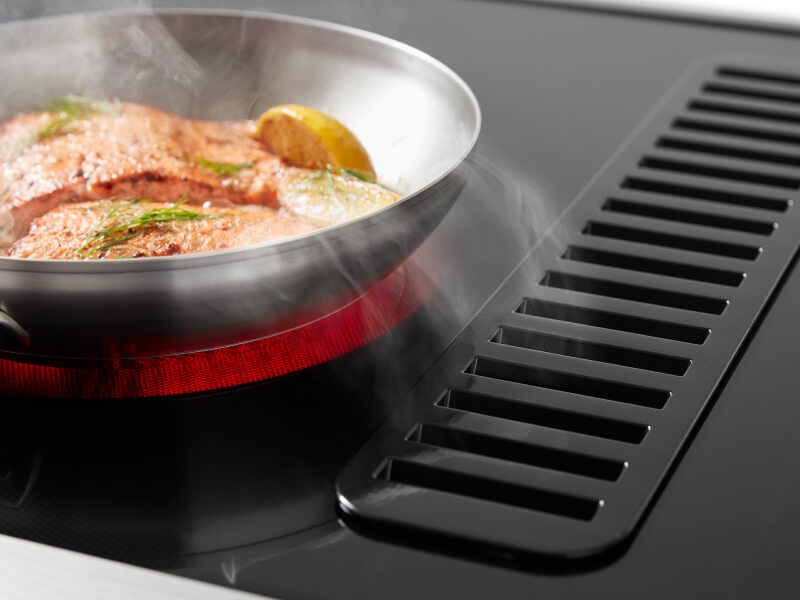 Salmon cooking on a downdraft electric range with a lit up red element 