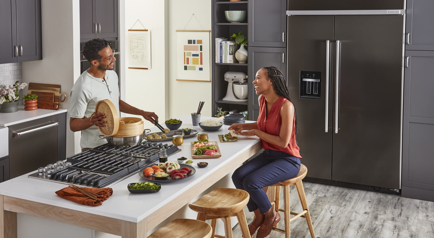 A man cooking for a woman on a downdraft gas cooktop set into a kitchen island