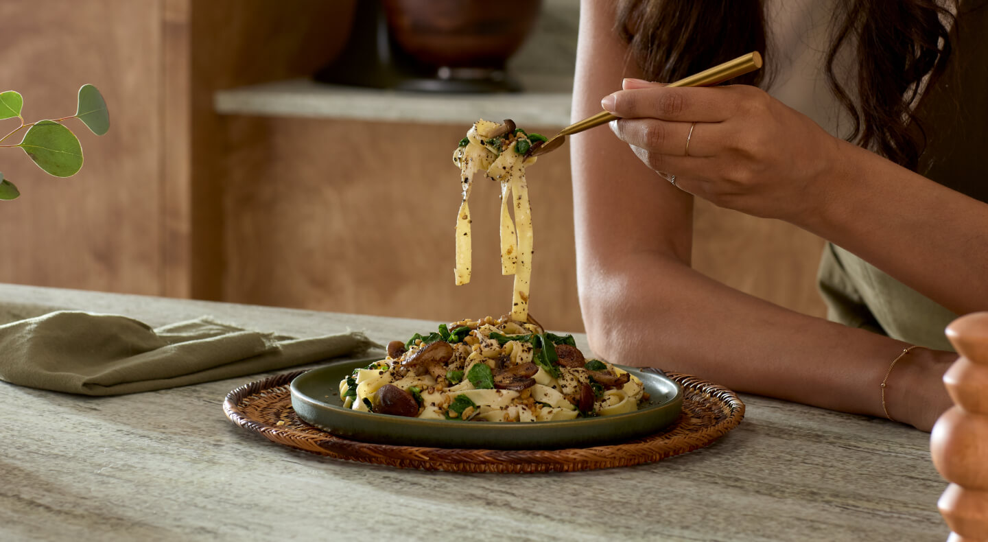Close-up of person eating noodle dish off of olive green plate