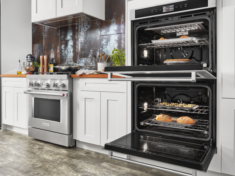 An opened KitchenAid® double oven next to a gas range