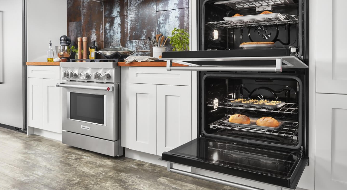 An opened KitchenAid® double oven next to a gas range