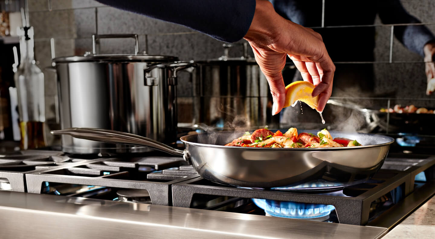 A person squeezing a lemon over cooking food on a cookto