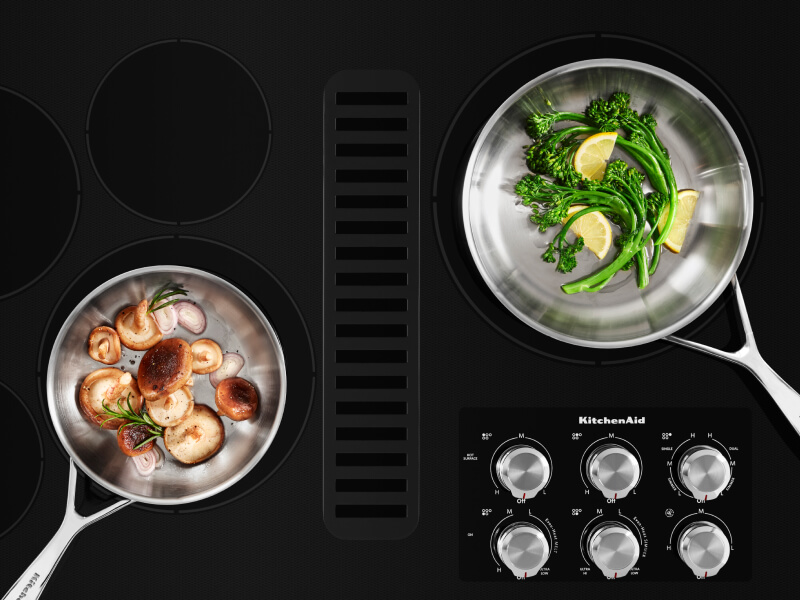 Two pans filled with vegetables on a cooktop