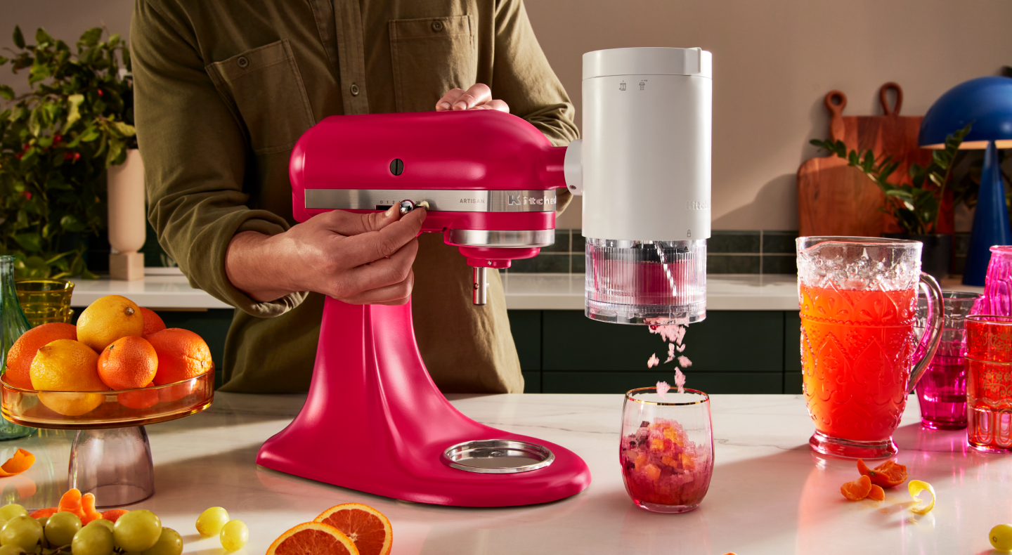 Pink KitchenAid® stand mixer with the KitchenAid®  Shave Ice Attachment shaving flavored ice into drink