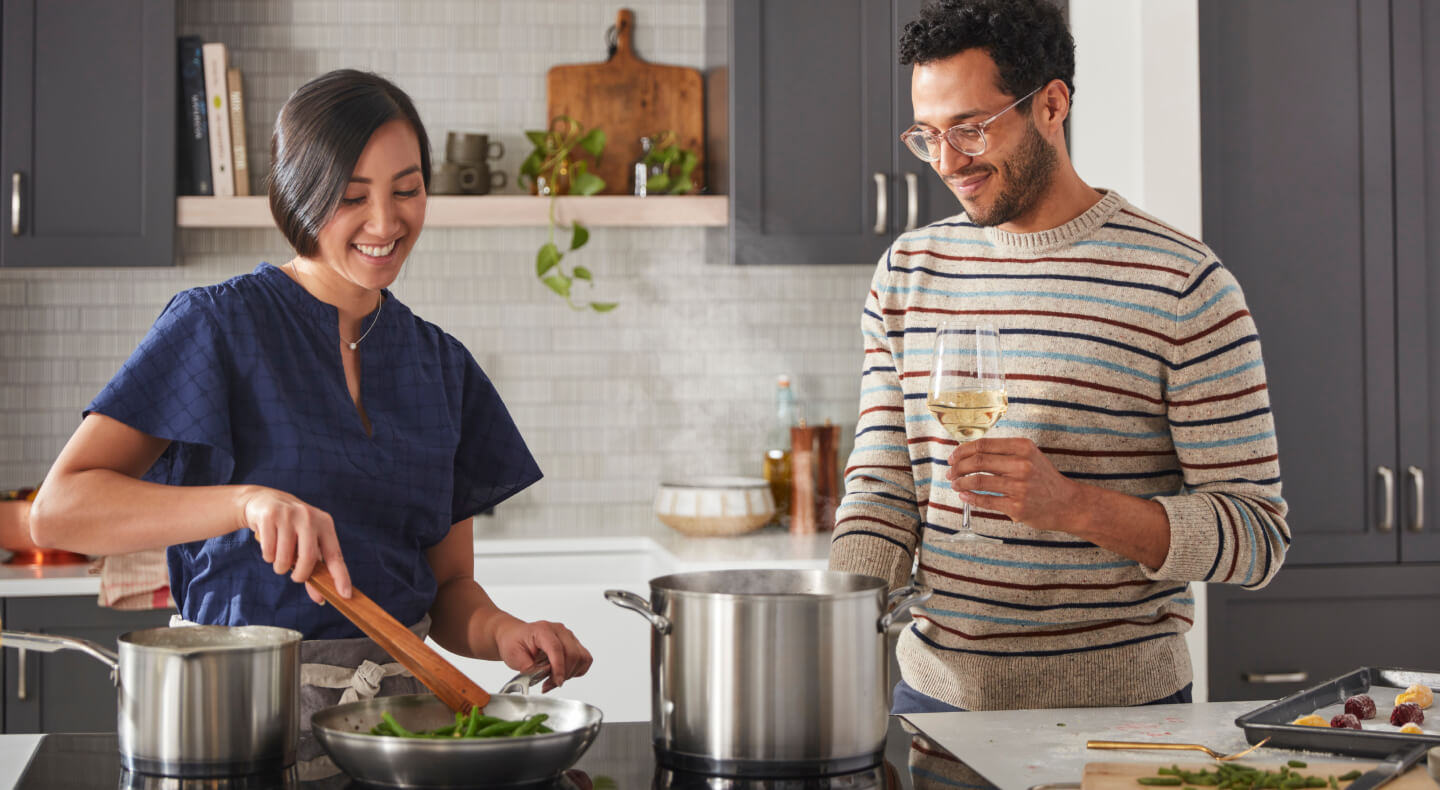 Two people cooking together using several stainless steel pans on an induction cooktop
