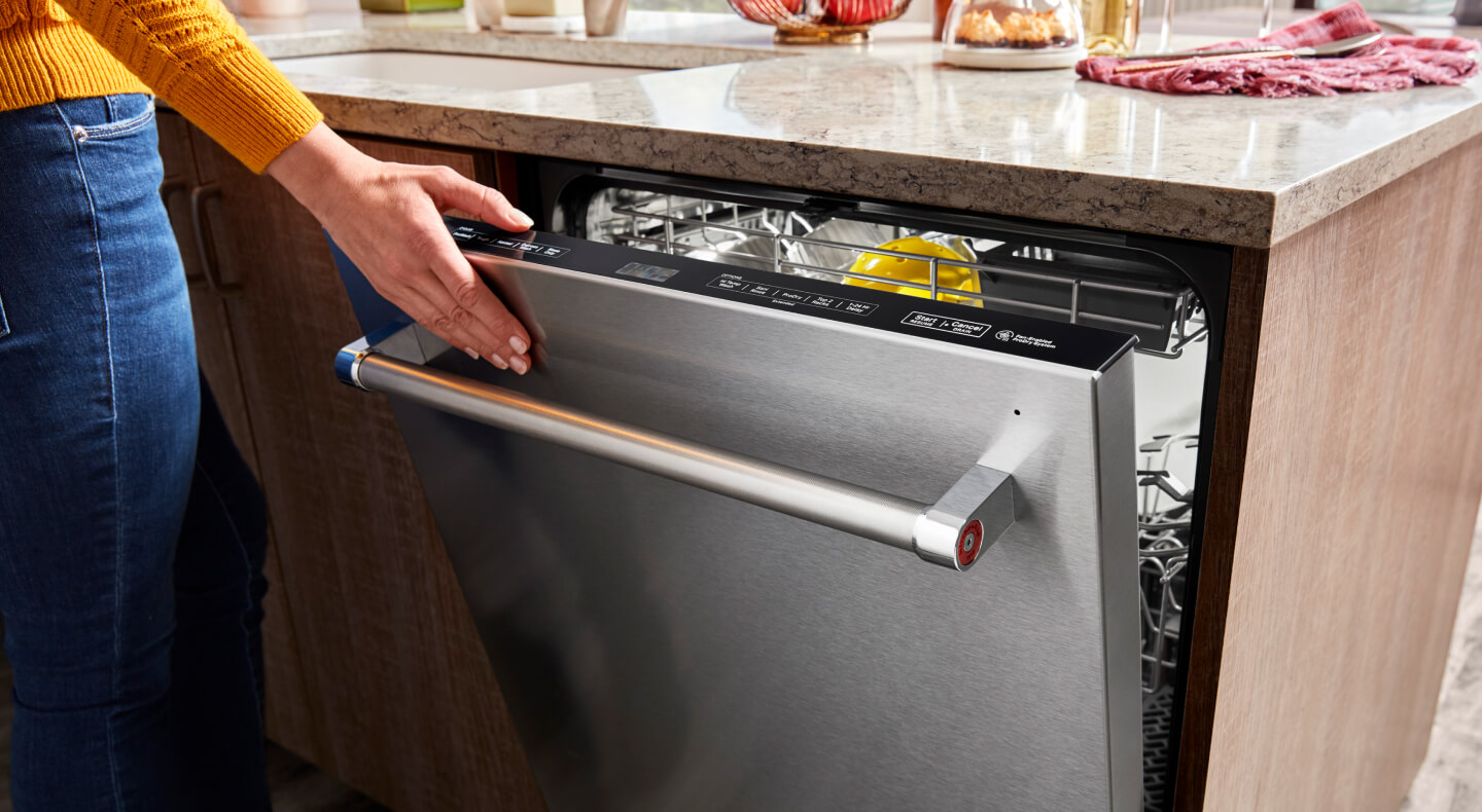 A hand closing a top control built-in dishwasher with a towel bar handle