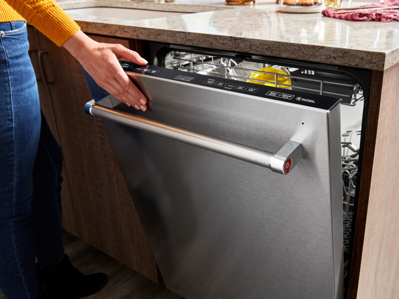 A hand closing a top control built-in dishwasher with a towel bar handle