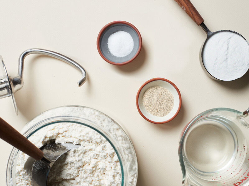 Ingredients for pizza dough next to a dough hook