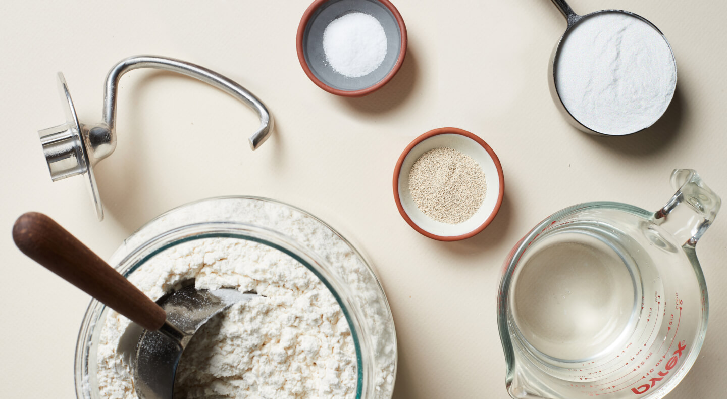 Ingredients for pizza dough next to a dough hook