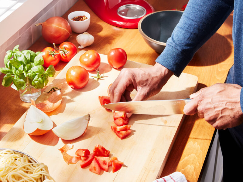 A person chopping tomatoes on a cutting board