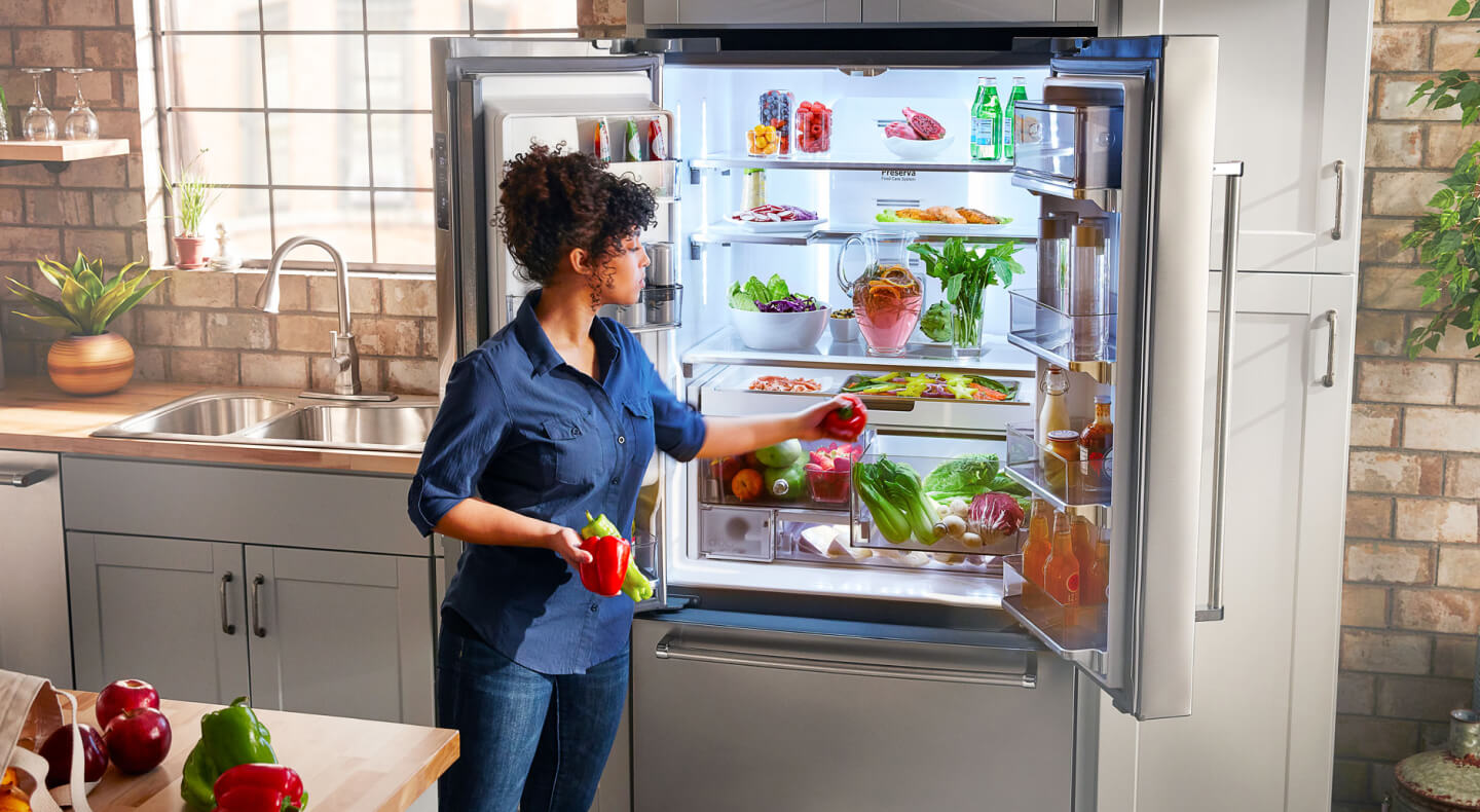 A person putting away fresh vegetables in a KitchenAid® french door refrigerator