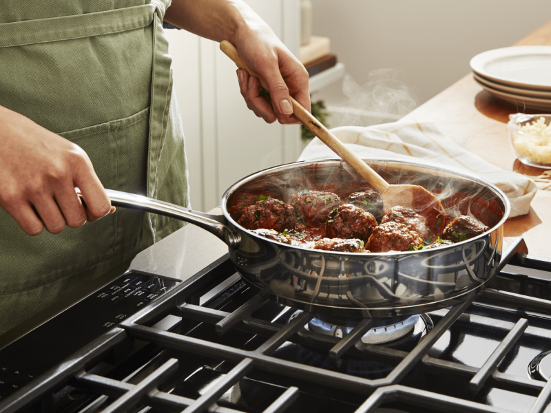 A person simmering vegan "meatballs" on a stovetop