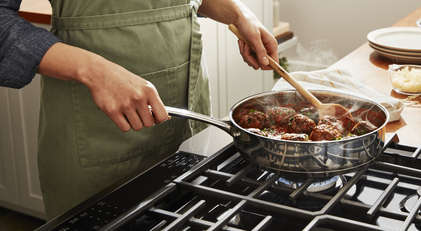 A person simmering vegan "meatballs" on a stovetop