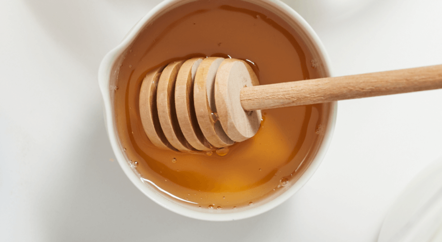 A honey dipper placed inside a bowl of vegan honey