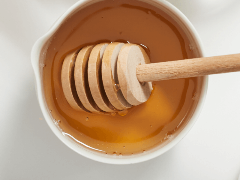 A honey dipper placed inside a bowl of vegan honey