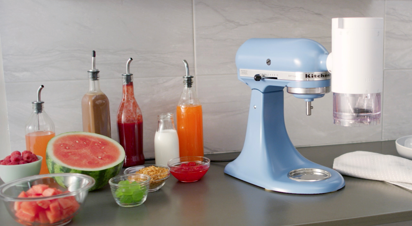 KitchenAid® stand mixer with shave ice attachment surrounded by syrups and fruit toppings