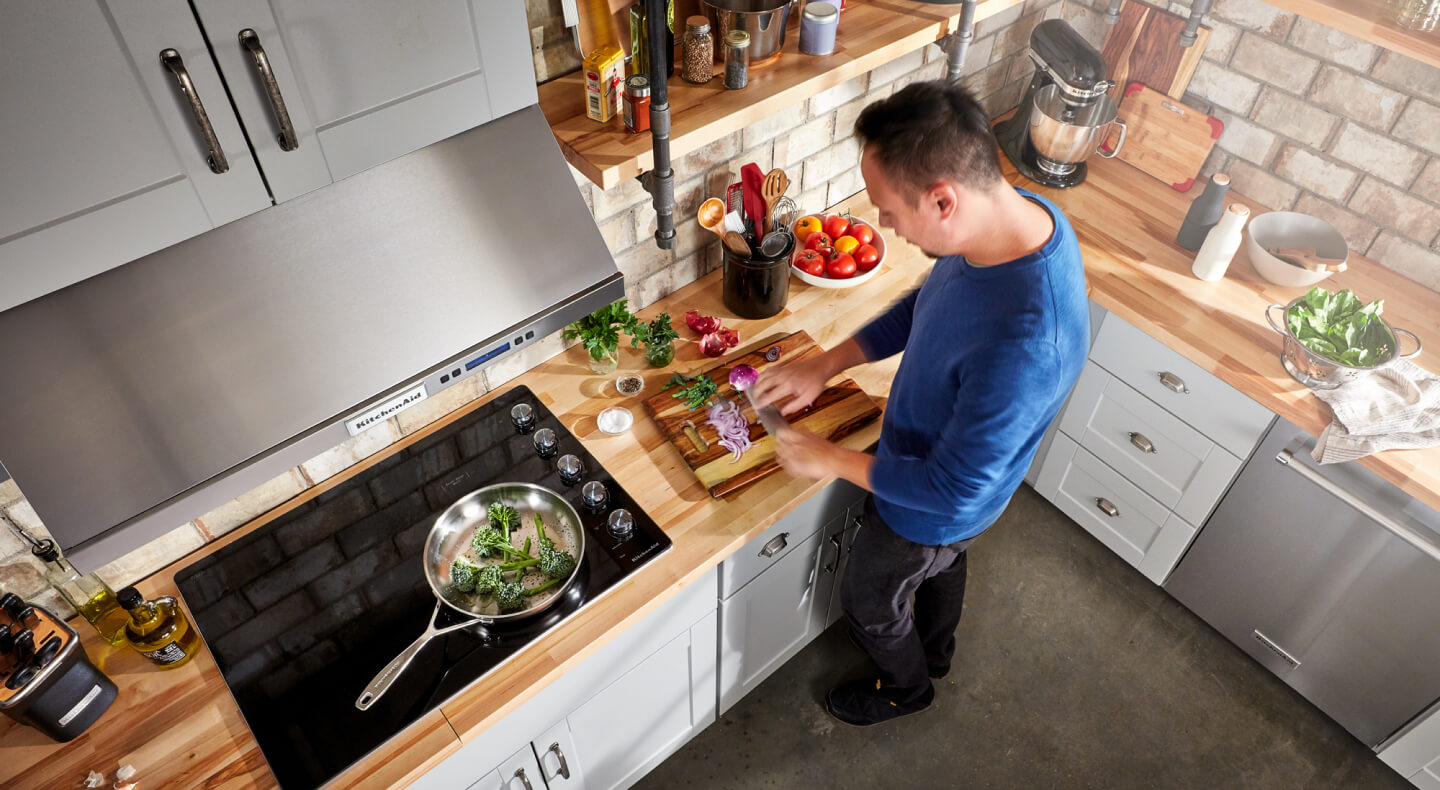 A person chopping vegetables next to their glass cooktop